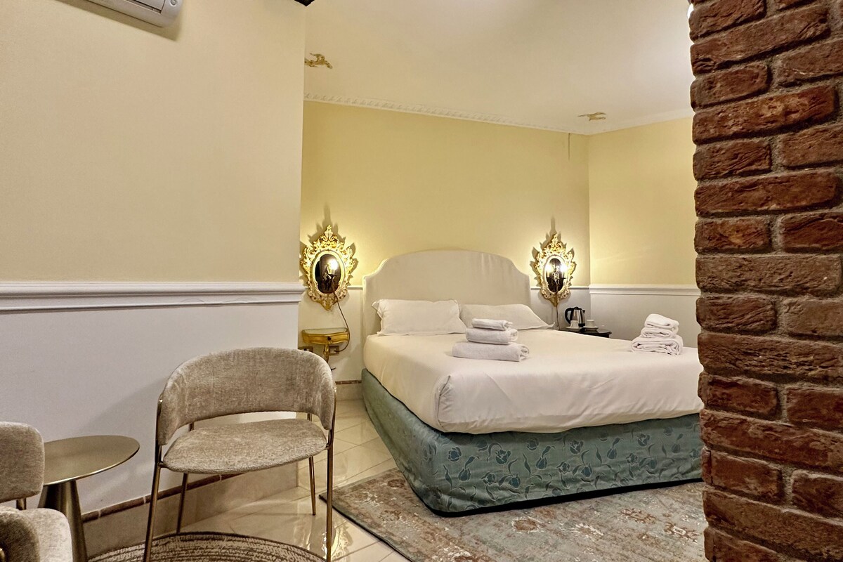 Una camera d'albergo con un letto, due sedie, un tavolino e una parete in mattoni.