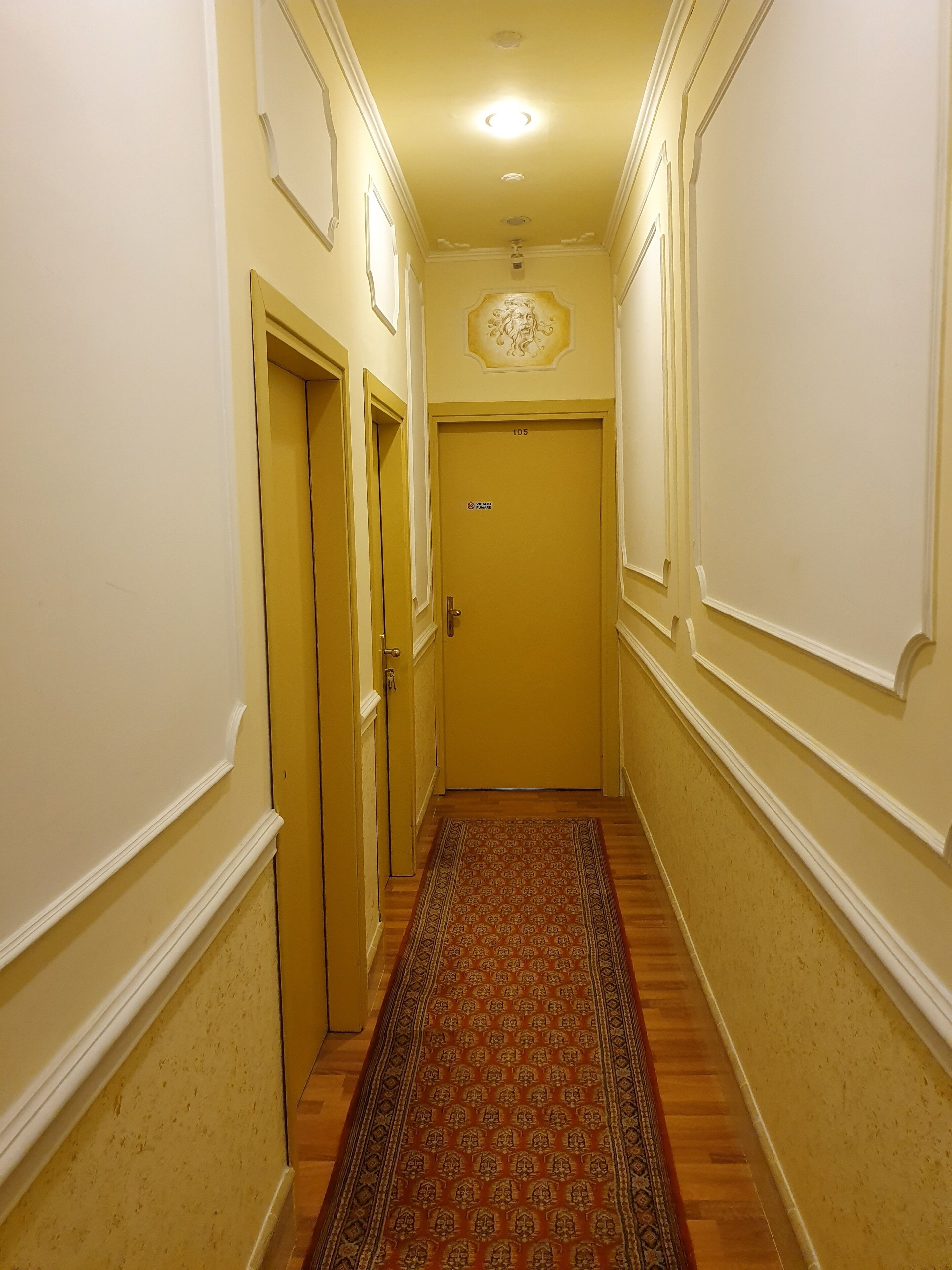 A narrow hallway with cream-colored walls, a patterned carpet, and a door marked "105".