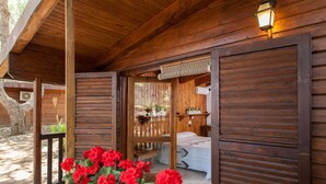 Une cabane en bois avec une véranda, un lit et un pot de fleurs contenant des fleurs rouges.
