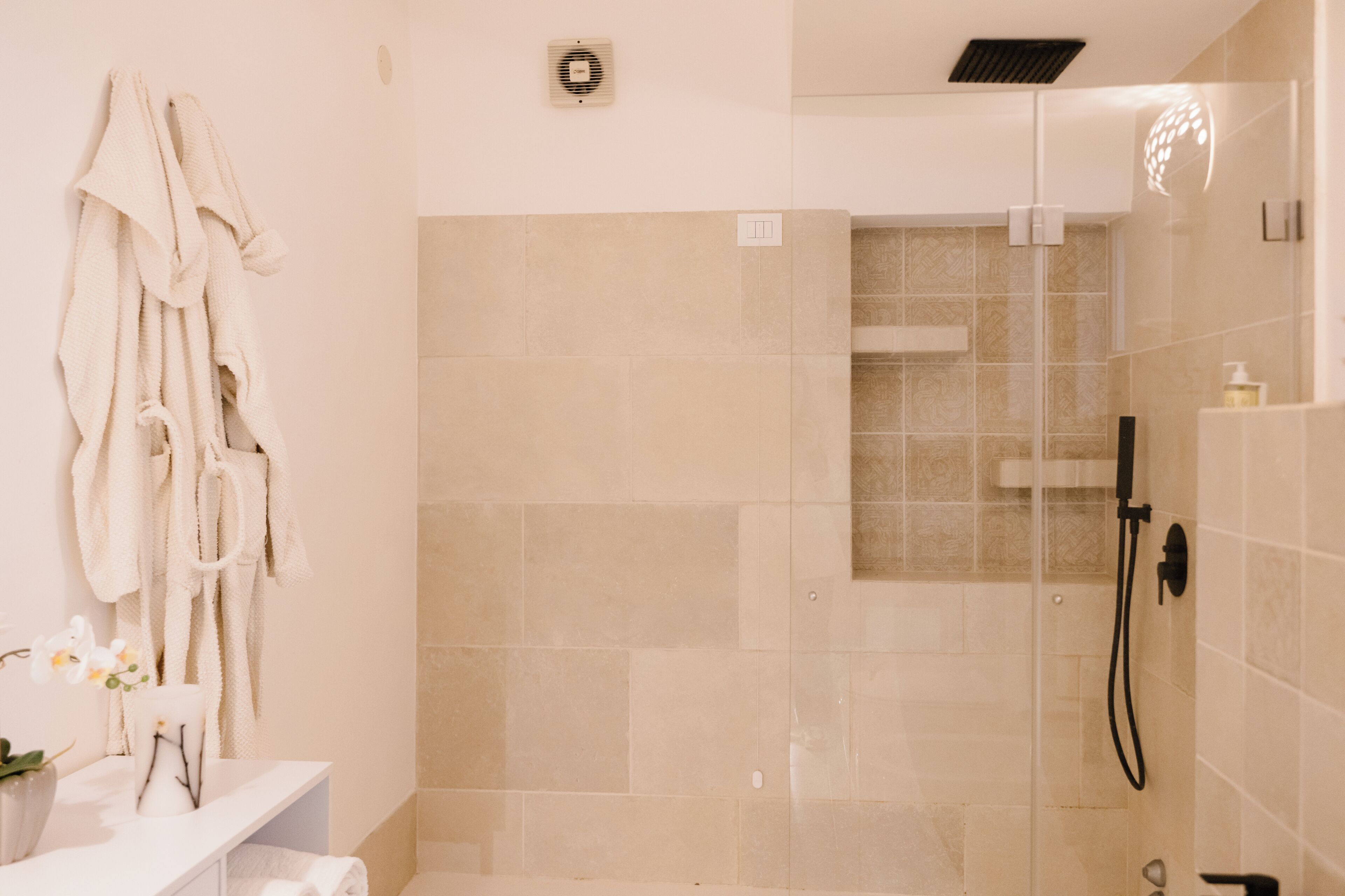 A bathroom with a shower, a towel rack with robes, and a small plant.