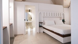 Une chambre à coucher comprenant un lit, une table de chevet, une étagère intégrée et une porte donnant sur une salle de bain.