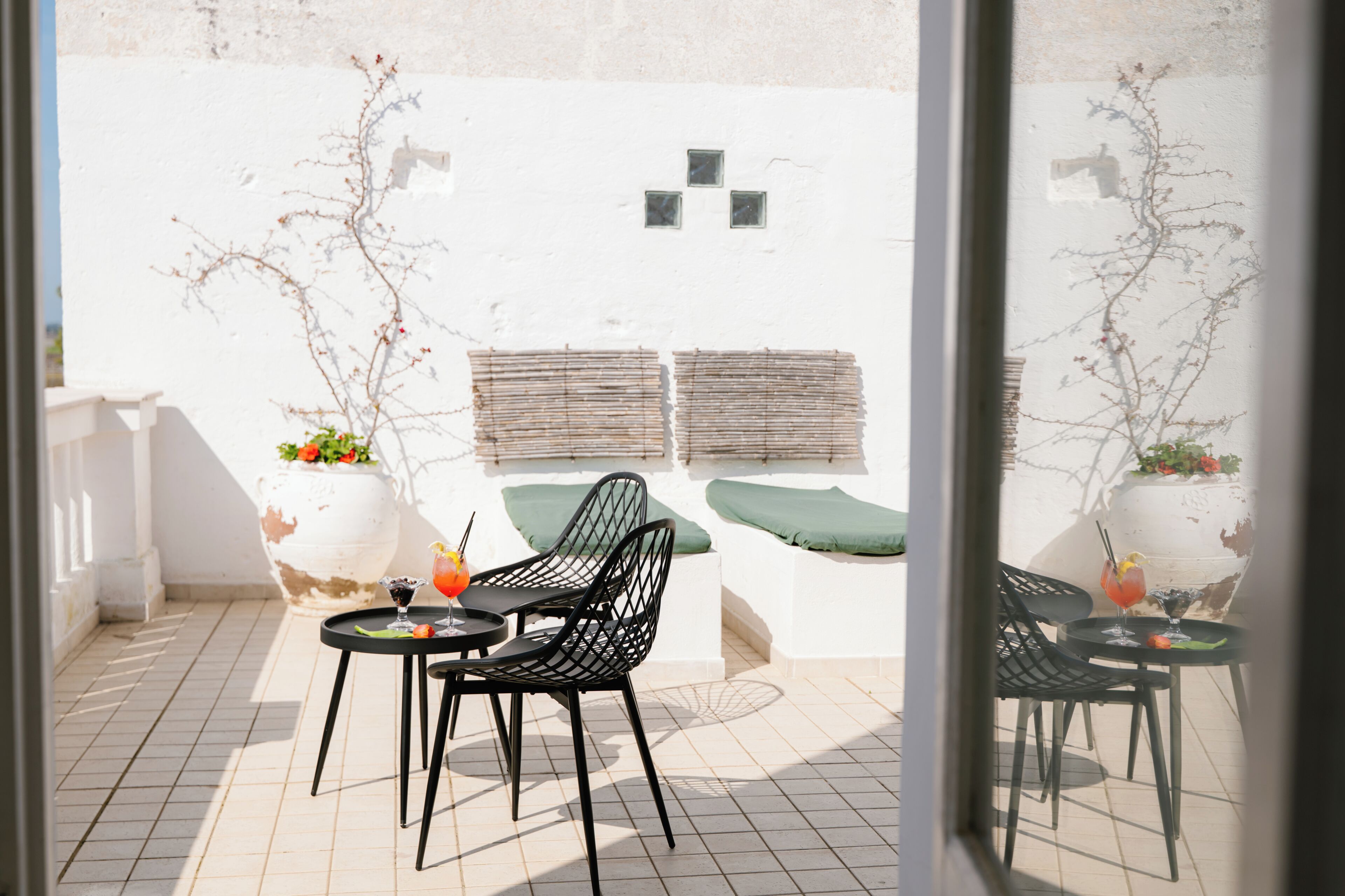 A patio with two tables, black chairs, and a white wall with a window and decorative elements.