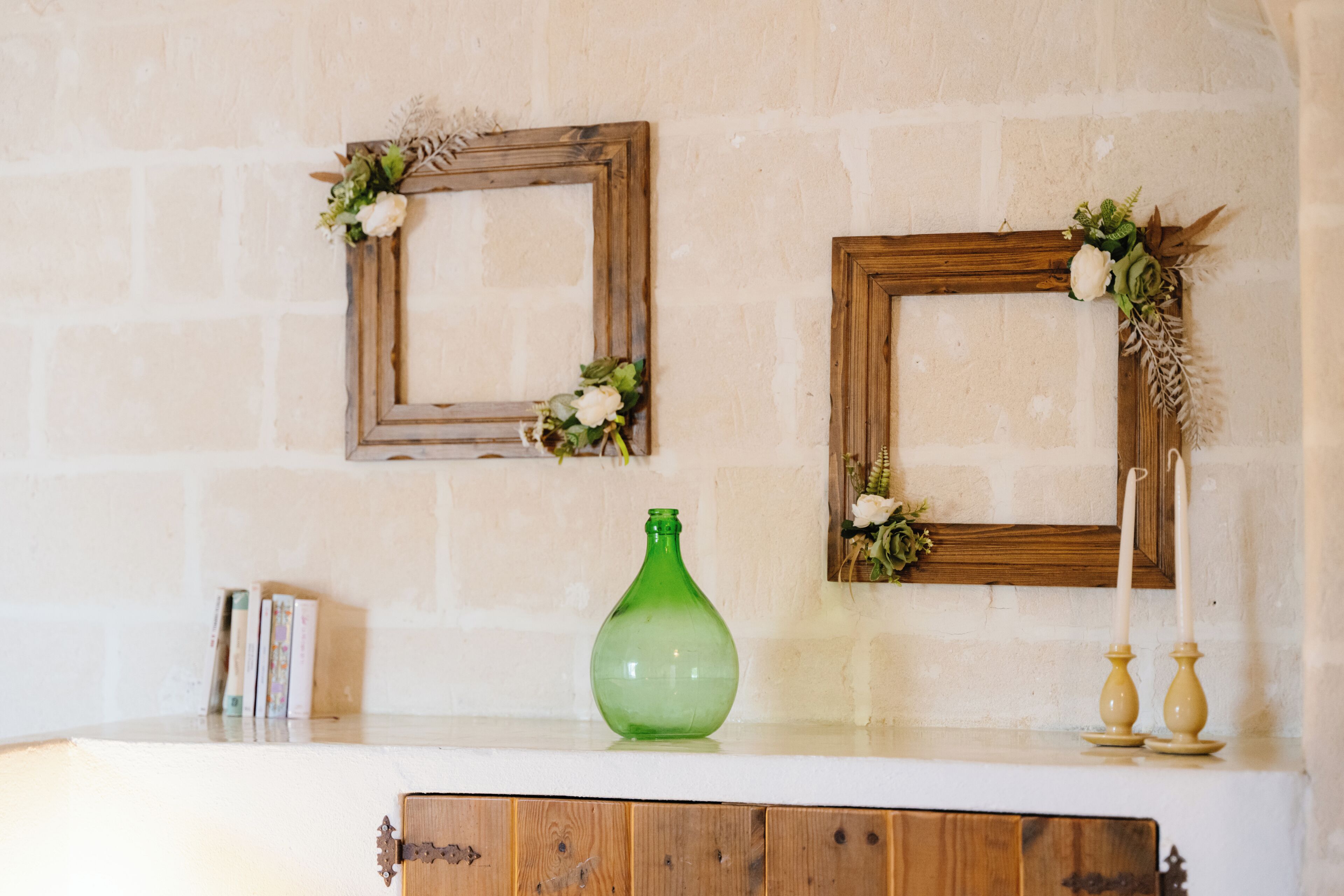 Un muro rustico con due quadri incorniciati, un vaso verde e portacandele.