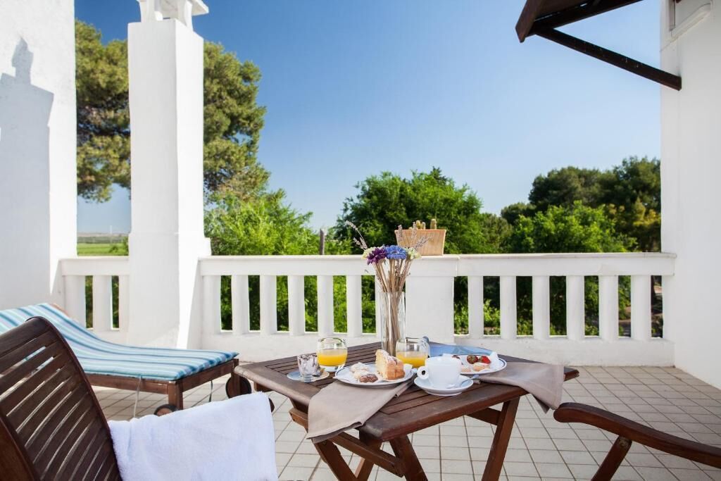 Une terrasse avec une table mise pour le petit-déjeuner, comprenant des assiettes, des verres et un vase avec des fleurs.