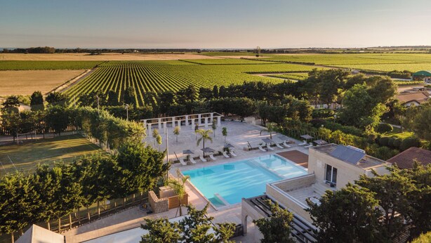 Un complexe hôtelier doté d’une piscine, de chaises longues et offrant une vue sur les champs agricoles.