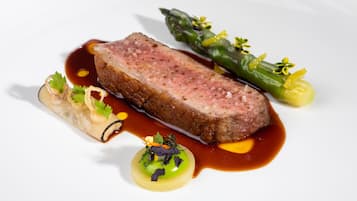 Un plato con una porción de carne, espárragos y un recipiente pequeño de salsa.