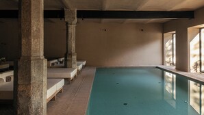 An indoor swimming pool with stone columns, benches, and a tiled floor.