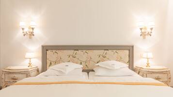 Un letto rifatto con lenzuola bianche e un dettaglio dorato, affiancato da due comodini con lampade.