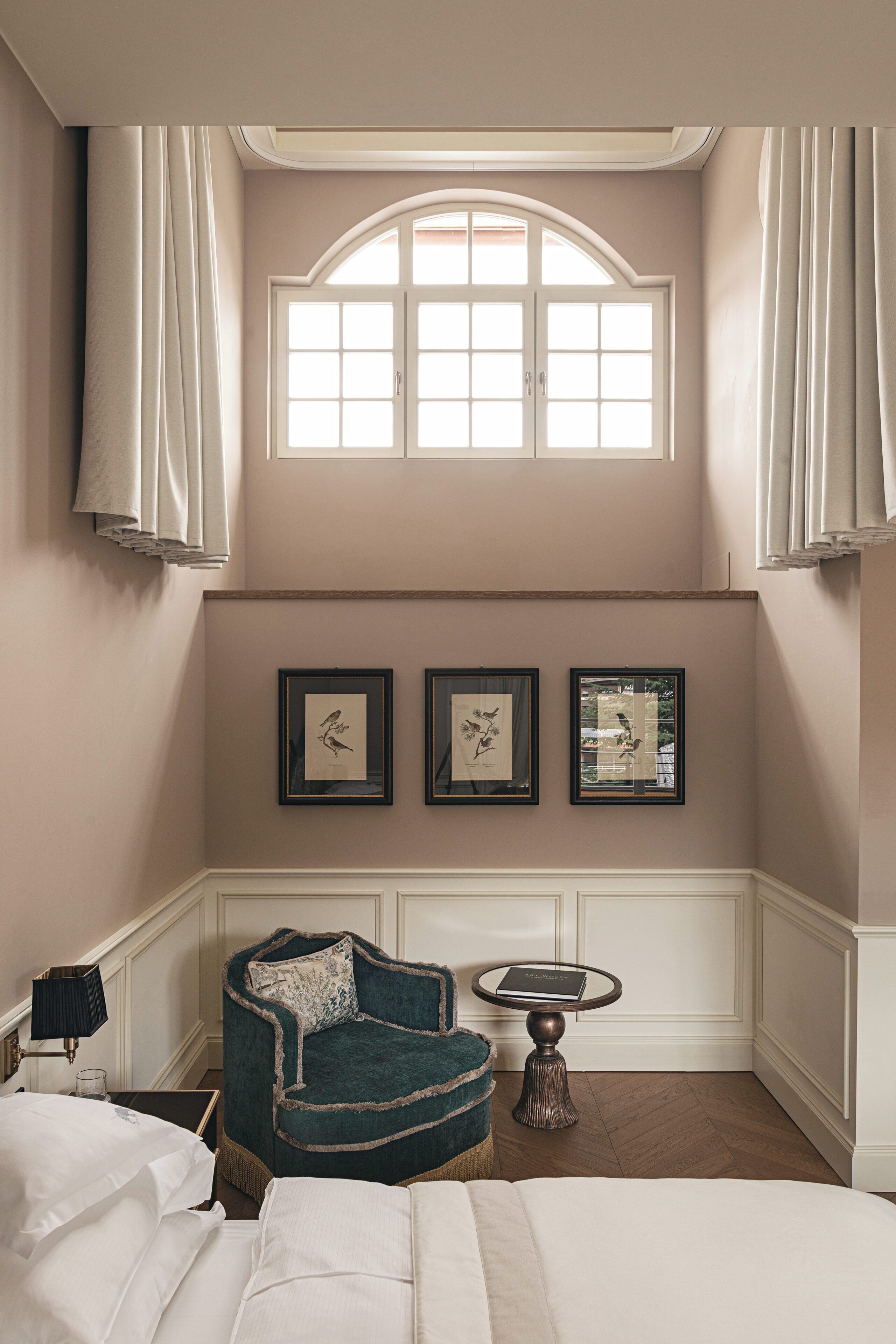 A bedroom with a bed, a chair, a small table, and a window with curtains.