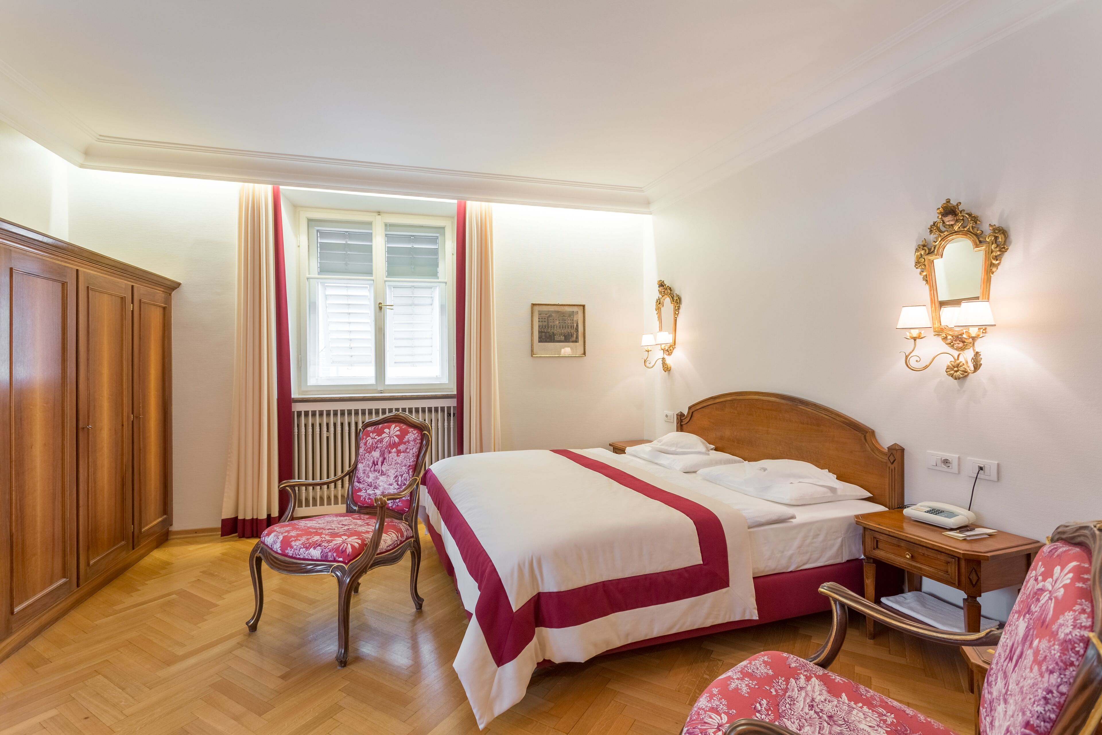 Ein Hotelzimmer mit Bett, Sessel, Nachttisch und einem Vorhangfenster.