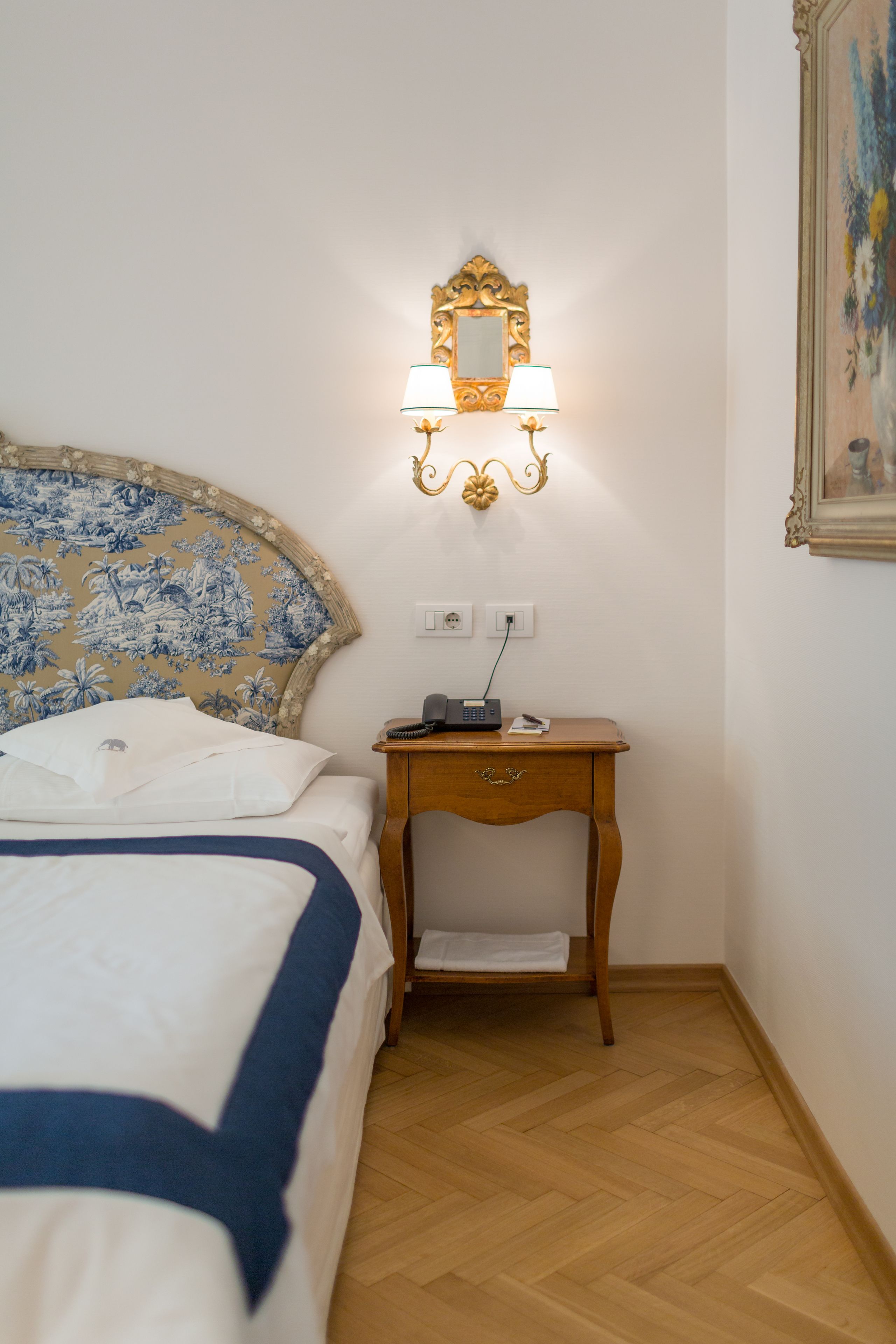 A hotel room with a bed, a nightstand with a lamp, and a mirror on the wall.