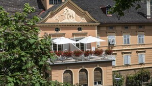 A building with a prominent elephant sculpture on the facade, arched windows, and a rooftop with umbrellas and flowers.
