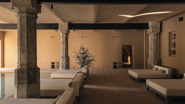 A room with a pool, stone columns, and a bed with a headboard.