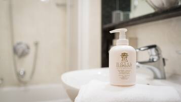 A bathroom with a white sink, a mirror, and a bottle of Hotel Elephant shampoo on a towel.