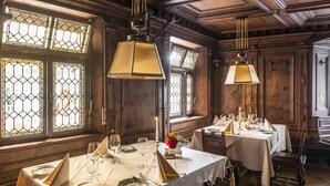 Un comedor con paredes de paneles de madera, amplias ventanas con vidrios de diseño tipo rombo y mesas dispuestas para una comida.