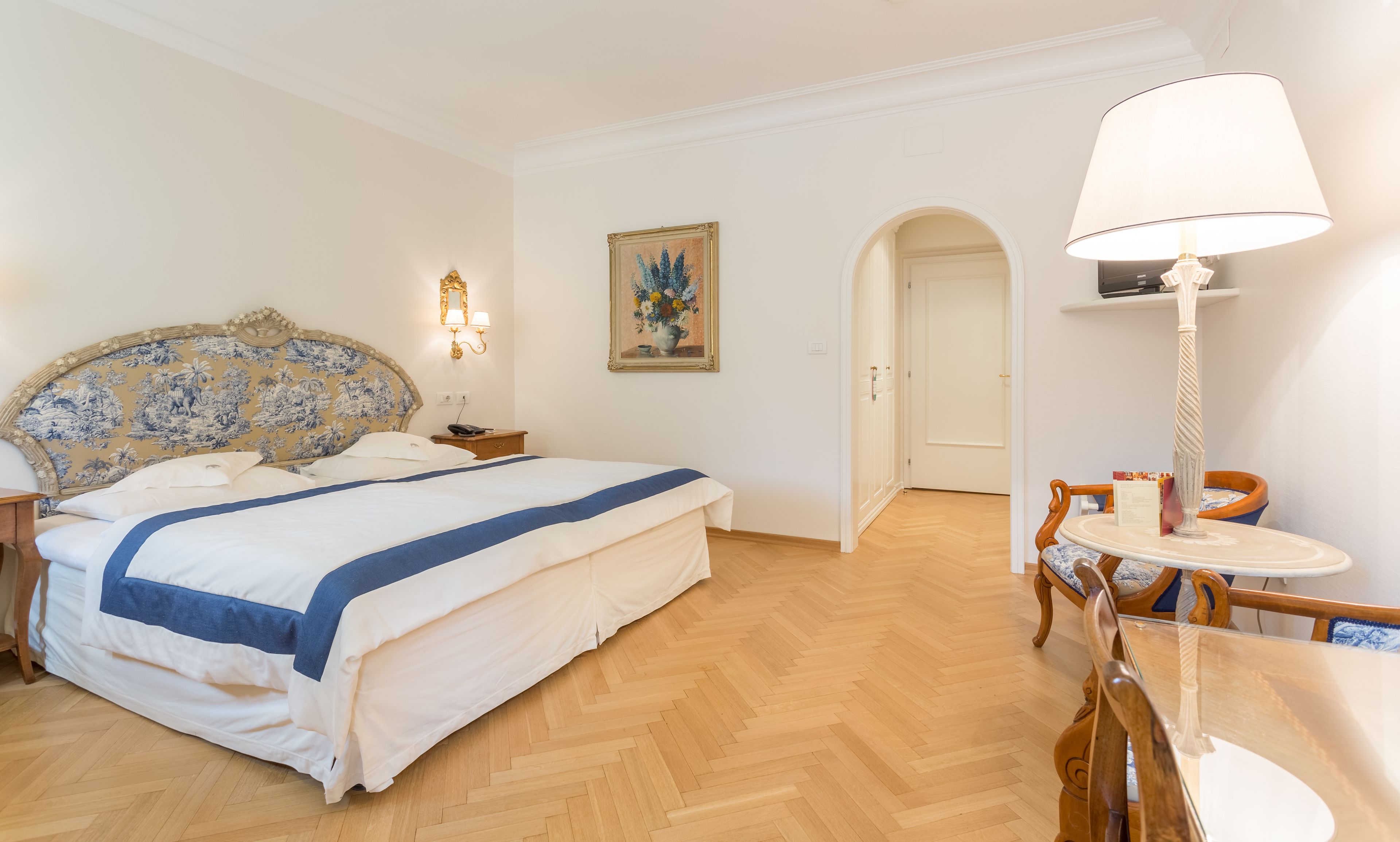 Una habitación de hotel con cama, escritorio, silla, lámpara y un cuadro en la pared.