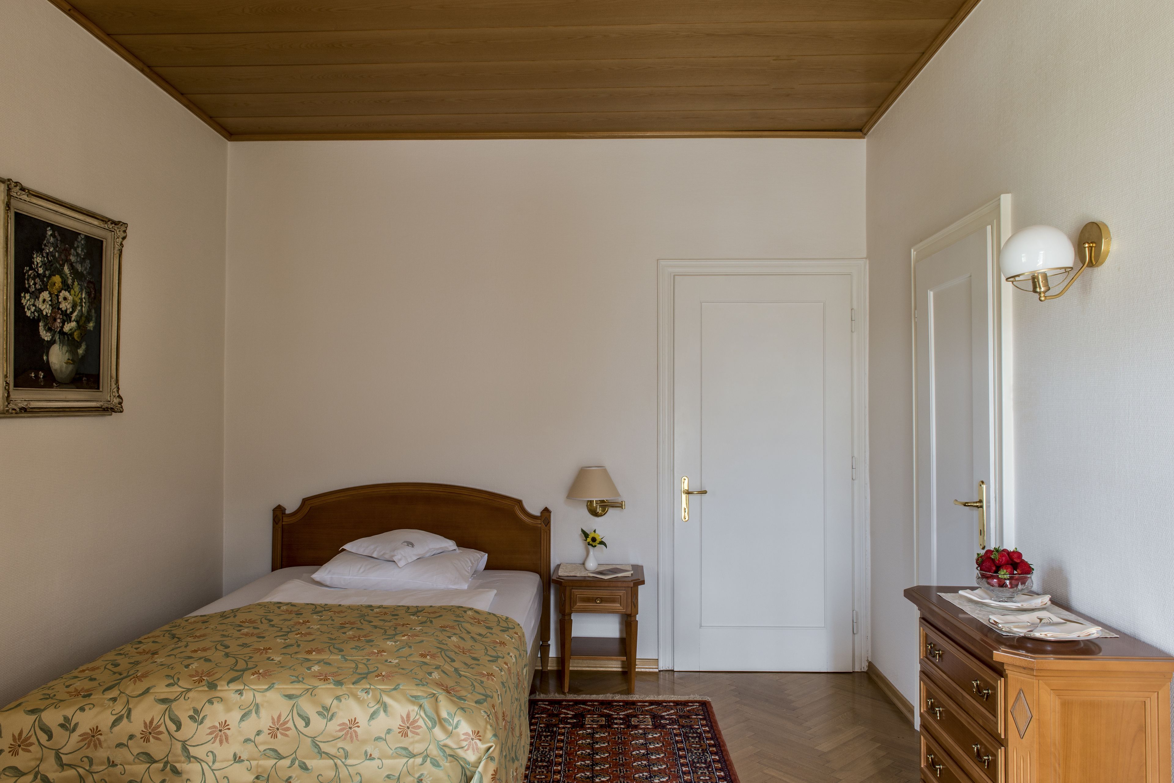 Un dormitorio con una cama de madera, una mesita de noche con lámpara, un aparador y una puerta.