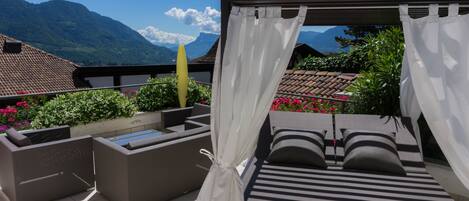 A balcony with a bed, seating area, and a view of mountains.