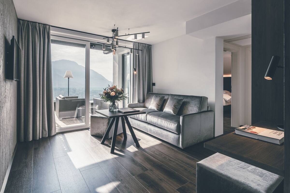 A modern living room with a sofa, a coffee table, and a view of mountains through large windows.