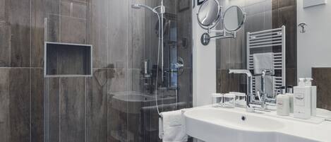 A modern bathroom with a glass-enclosed shower, a white sink with toiletries, and a large mirror.