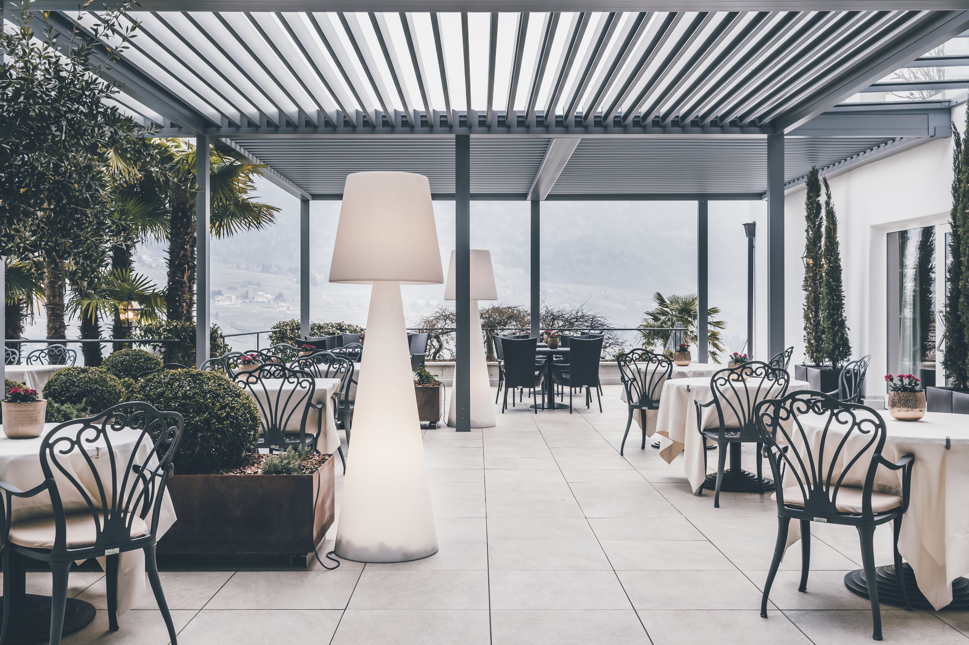 Un espace extérieur aménagé en terrasse, avec des tables et des chaises, de grandes lampes et des plantes en pot.