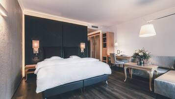 Una habitación de hotel moderna con una cama grande, mesitas de noche, un escritorio y un sofá.