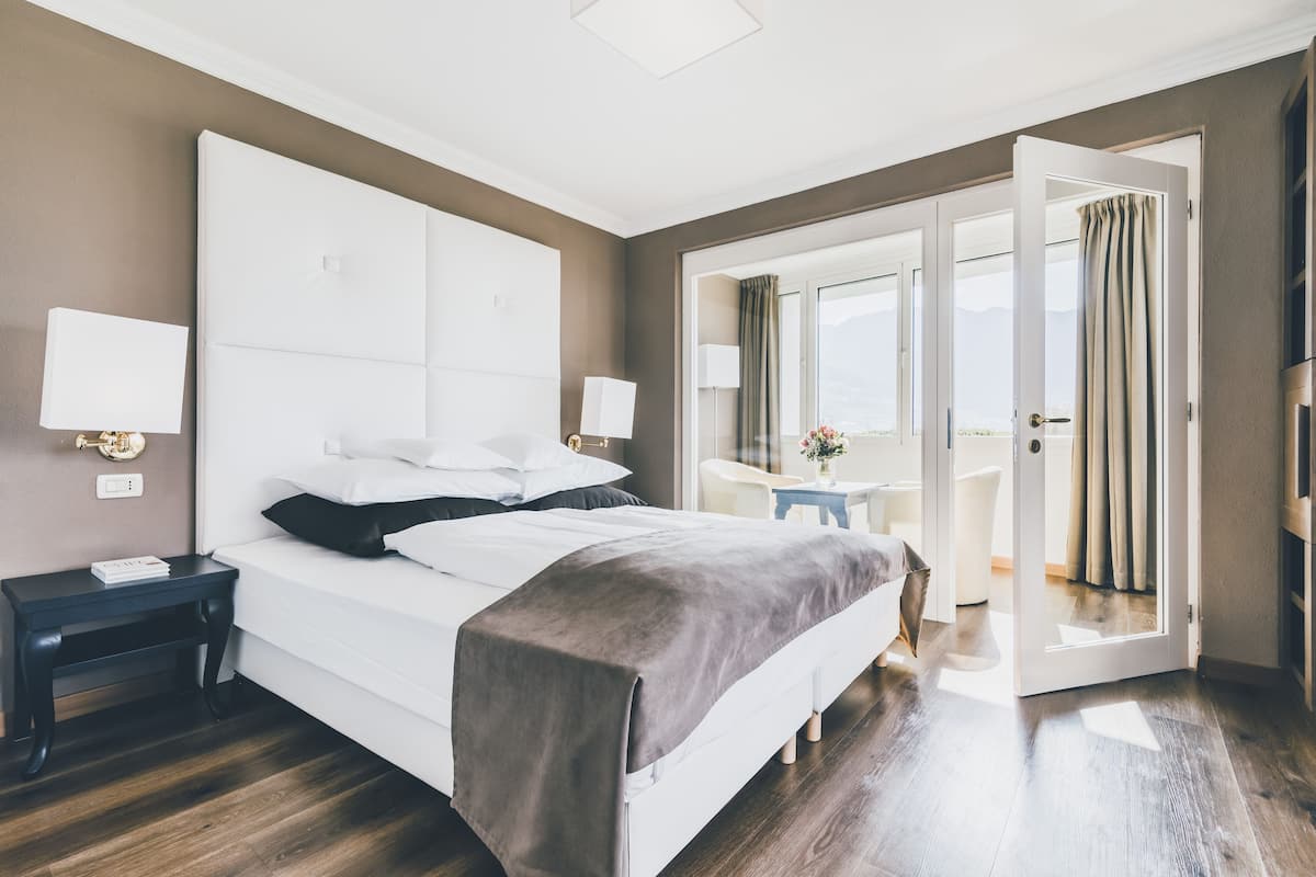 A modern hotel room with a large bed, bedside tables, a desk, and a view through an open door.