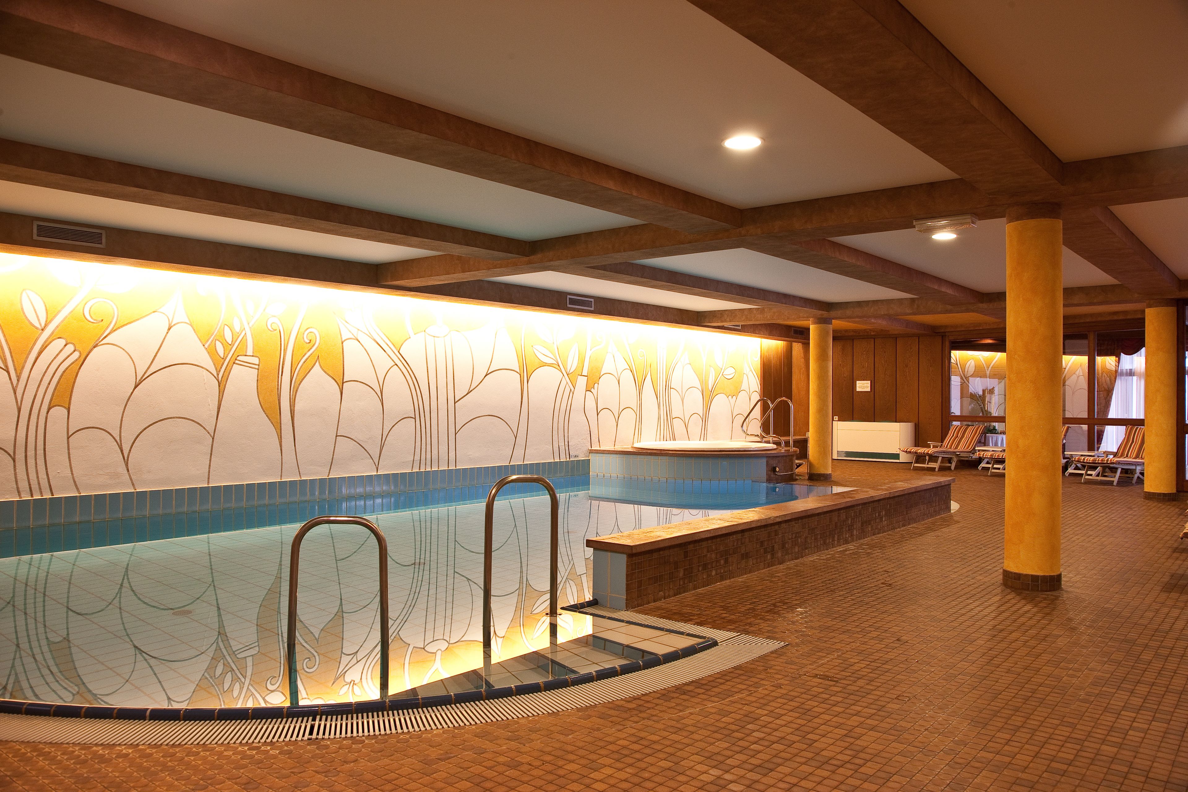 Una piscina interior con un muro decorativo, sillones de descanso y suelo de baldosas.