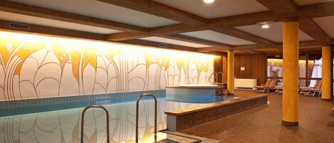 Una piscina interior con un muro decorativo, sillones de descanso y suelo de baldosas.