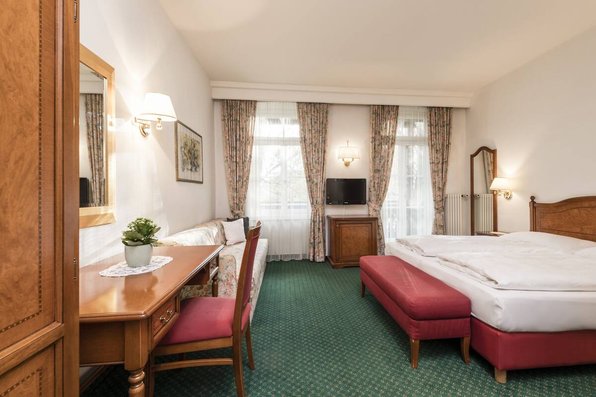 A hotel room with a bed, a desk, a chair, a television, and a window with curtains.