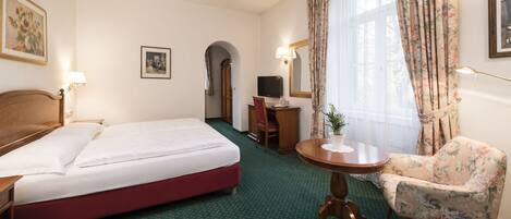 A hotel room with a bed, a desk, a chair, a television, and a window with curtains.