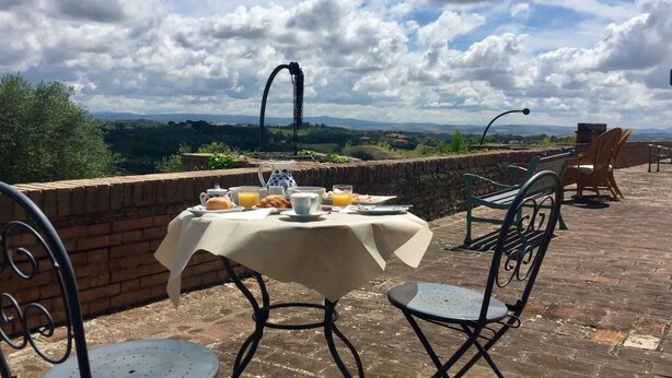 A table set for breakfast with a scenic view of hills and a cloudy sky. - Palazzo di Valli (Siena)