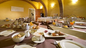 A breakfast buffet with various food items and beverages, set in a room with arched ceilings and yellow walls. - Palazzo di Valli (Siena)