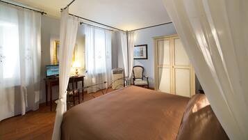 A hotel room with a bed, a desk with a lamp, a chair, and a wardrobe.