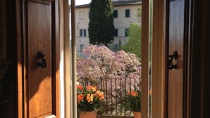 An open wooden door leading to a courtyard with potted plants and a view of buildings in the background. - Palazzo di Valli (Siena)