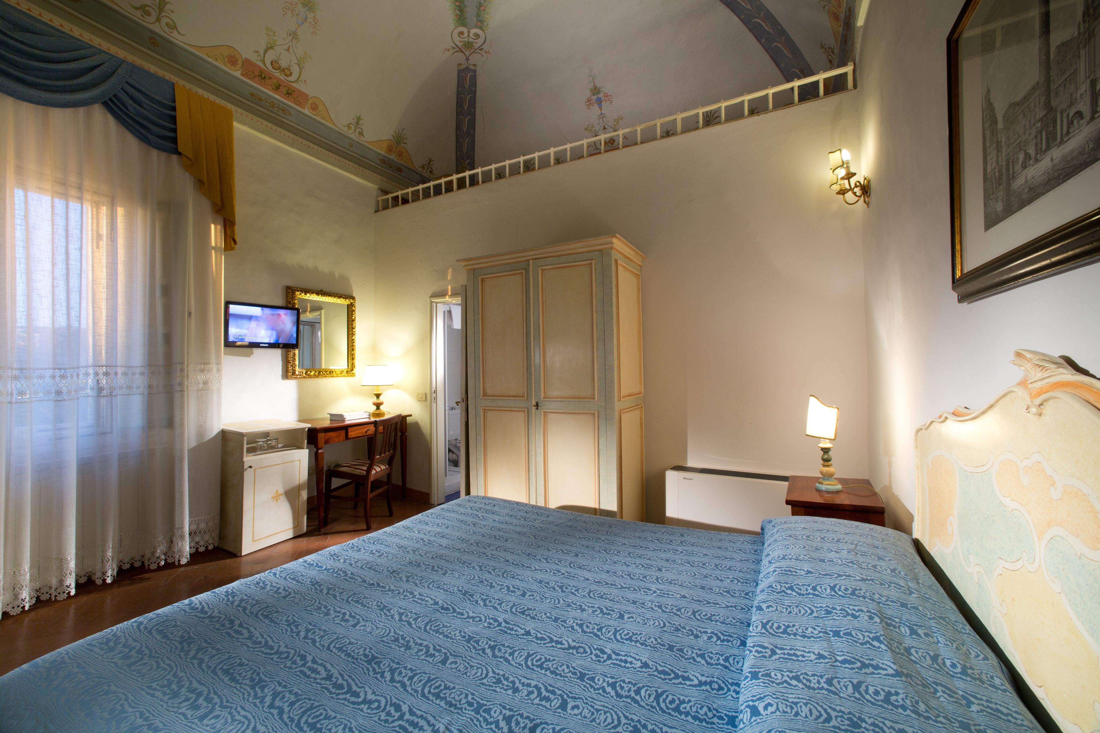 Une chambre d’hôtel avec un grand lit, un bureau avec une télévision, une armoire et un tableau au mur.