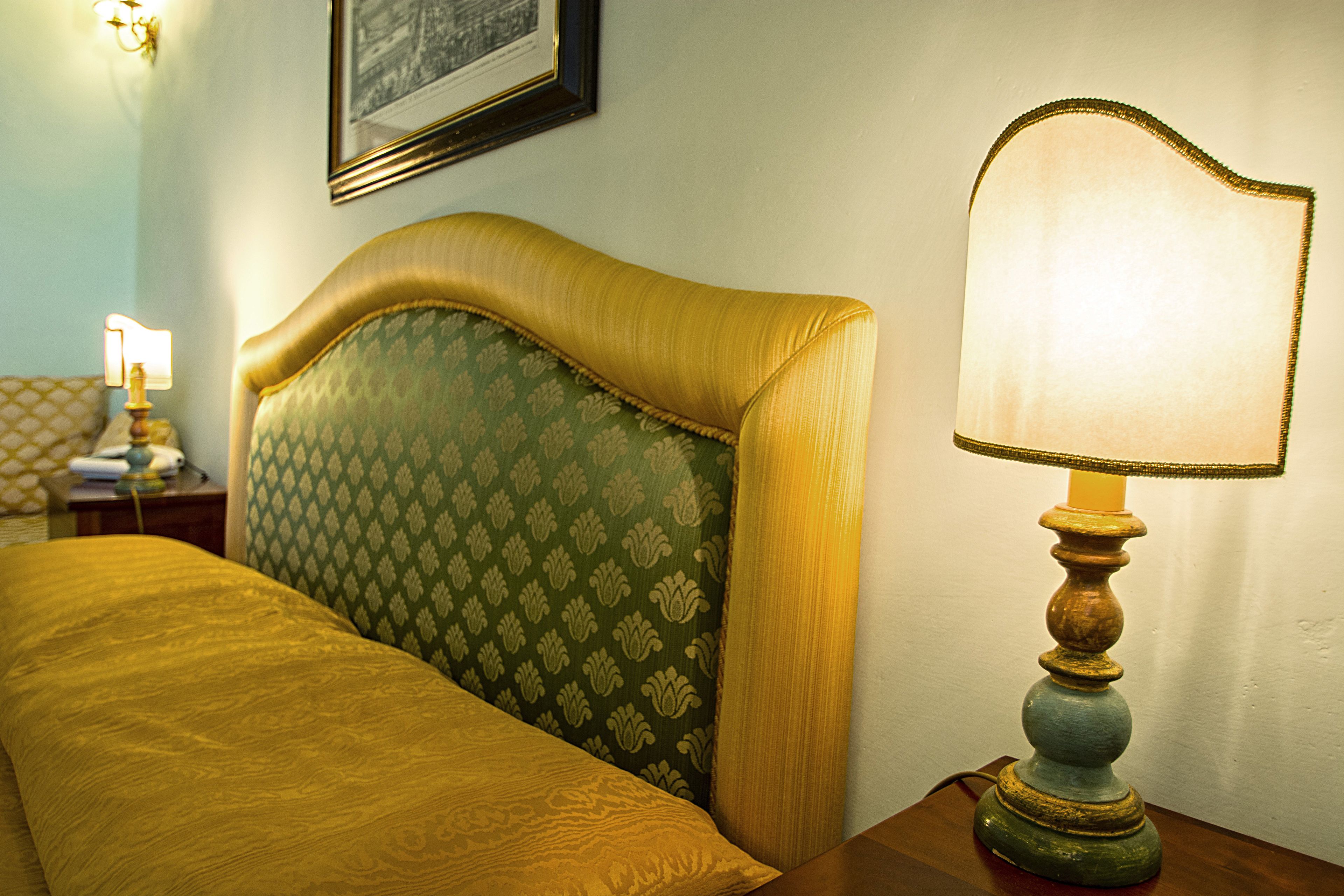 A neatly made bed with a green patterned headboard, a wooden nightstand with a lamp, and a framed picture on the wall.