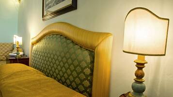A neatly made bed with a green patterned headboard, a wooden nightstand with a lamp, and a framed picture on the wall.