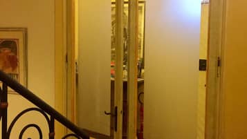 A hallway with a double door, a staircase with ornate metal railings, and a framed picture on the wall.