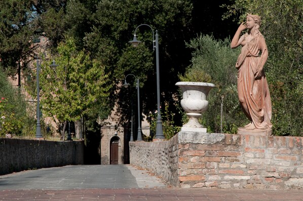A statue on a pedestal in a garden with a stone wall and trees in the background. - Palazzo di Valli (Siena)