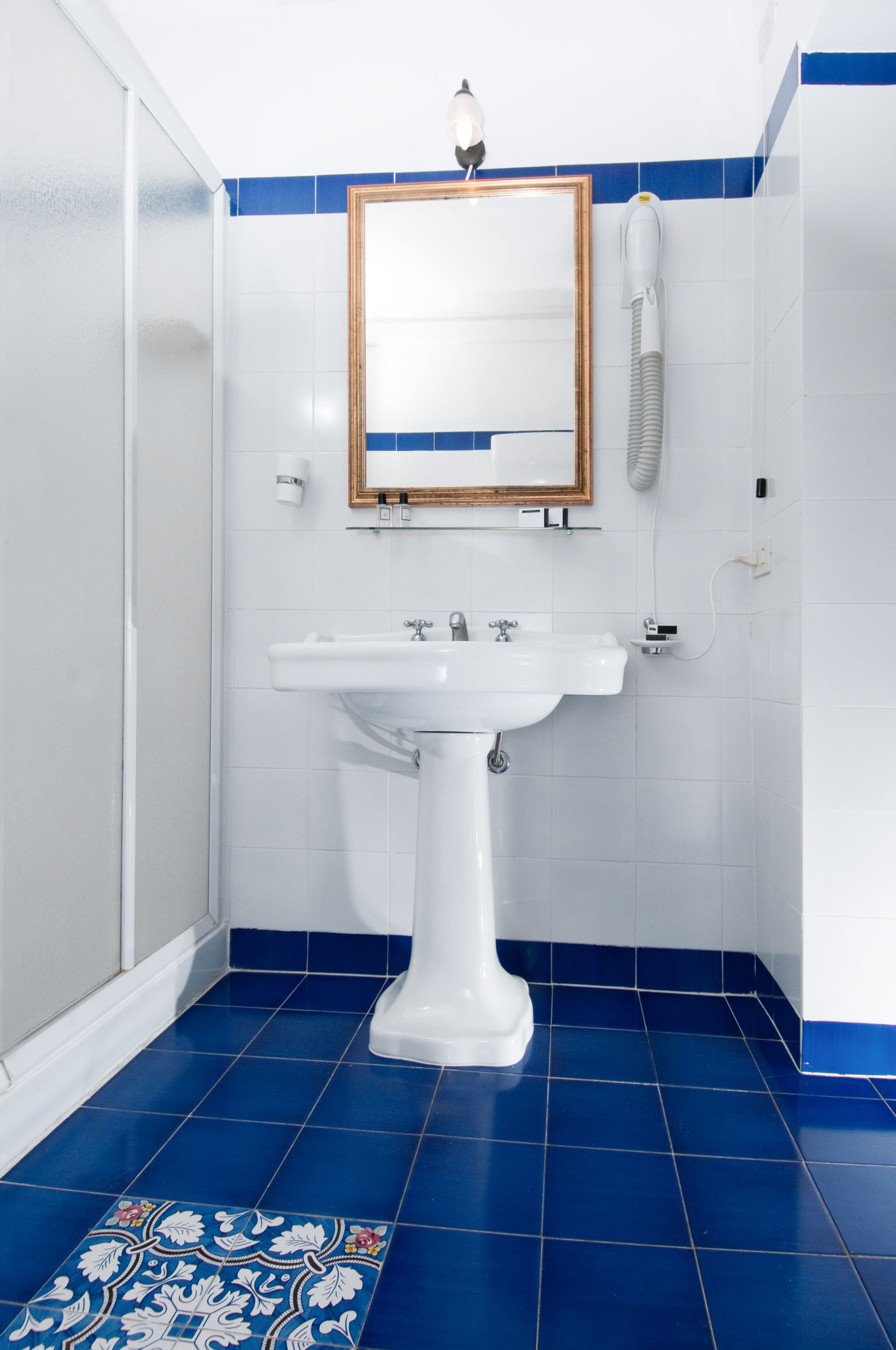 A bathroom with a white sink, blue-tiled floor, and a mirror with a wooden frame.