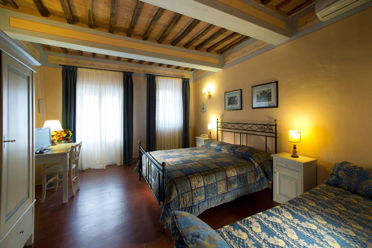 A hotel room with a wooden ceiling, a bed with a patterned bedspread, a desk with a lamp, and a chair.