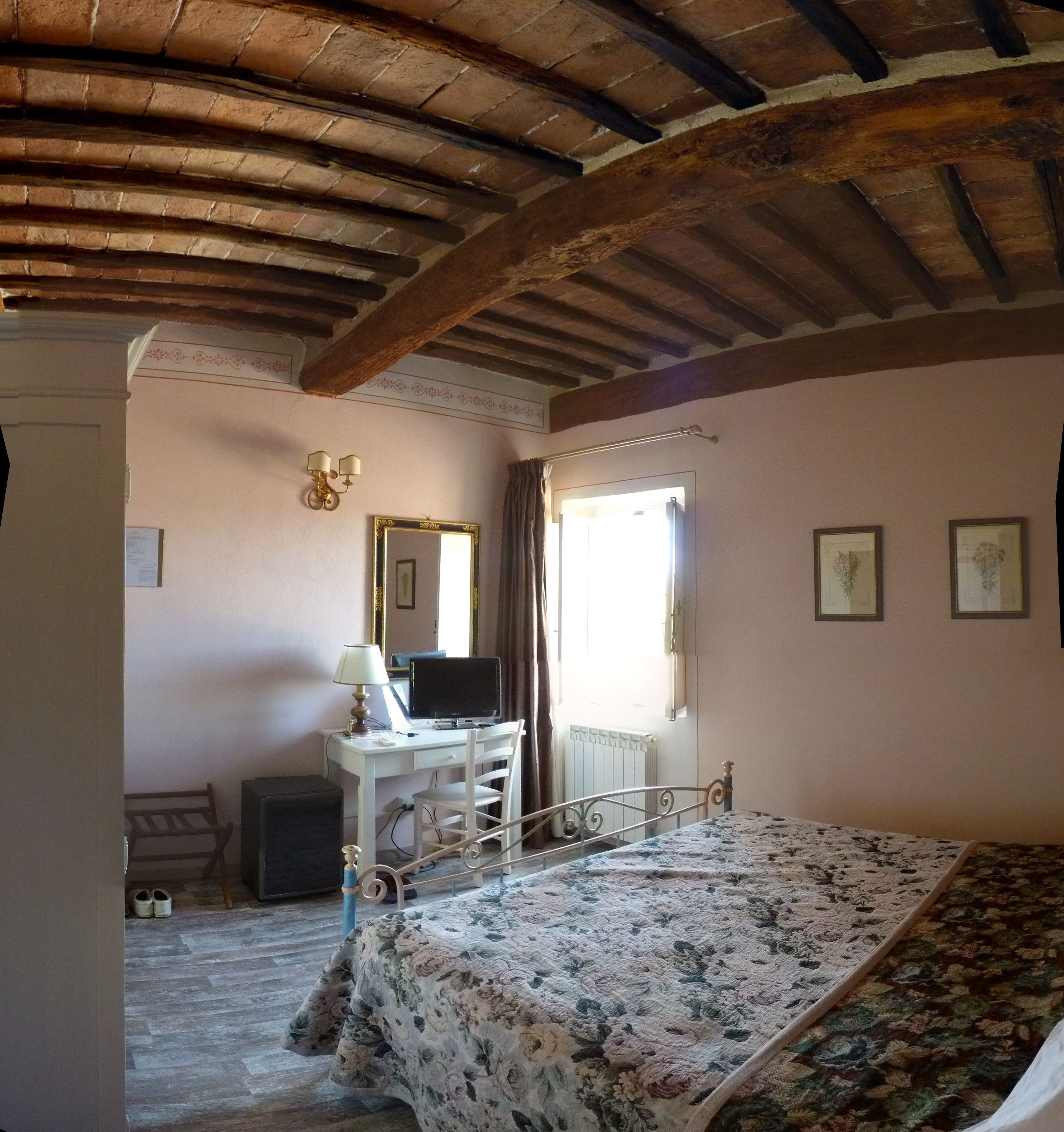 Un dormitorio con cama, escritorio con computadora, silla, lámpara, espejo y ventana con cortinas.