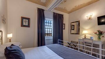 A hotel room with a bed, a desk, a chair, a lamp, a mirror, and a window with curtains.