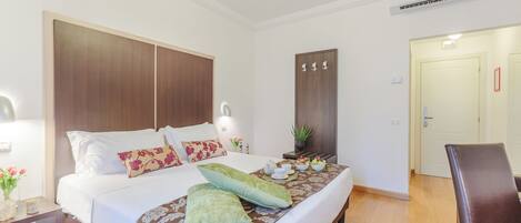 Une chambre d’hôtel avec un grand lit, une table de chevet avec une lampe, une chaise et une porte.