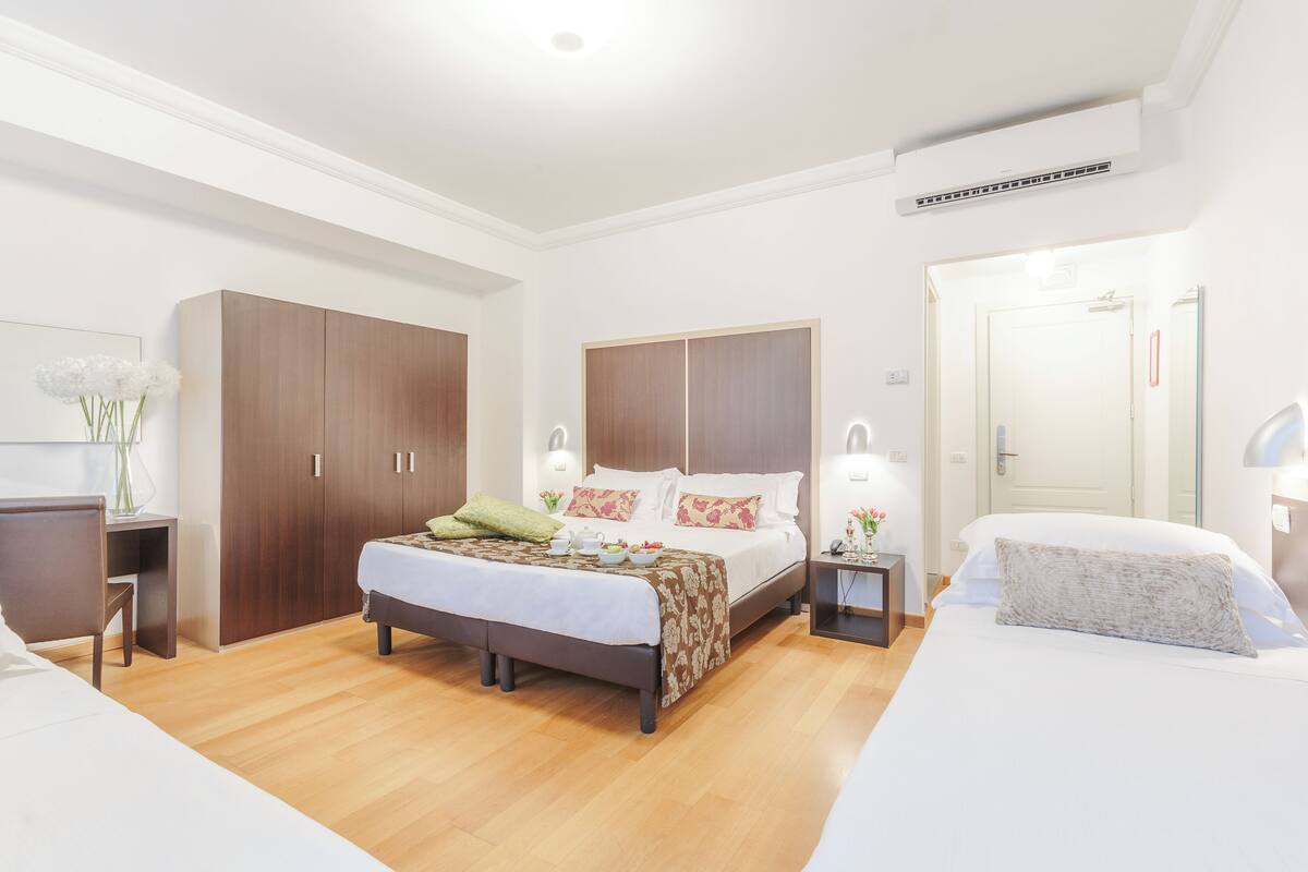 A modern bedroom with a large bed, a desk, and a wardrobe.
