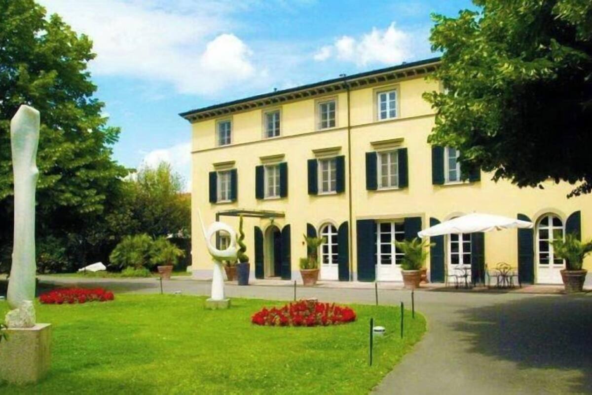 A two-story building with a symmetrical facade, large windows with shutters, and a well-maintained lawn with red flowers.