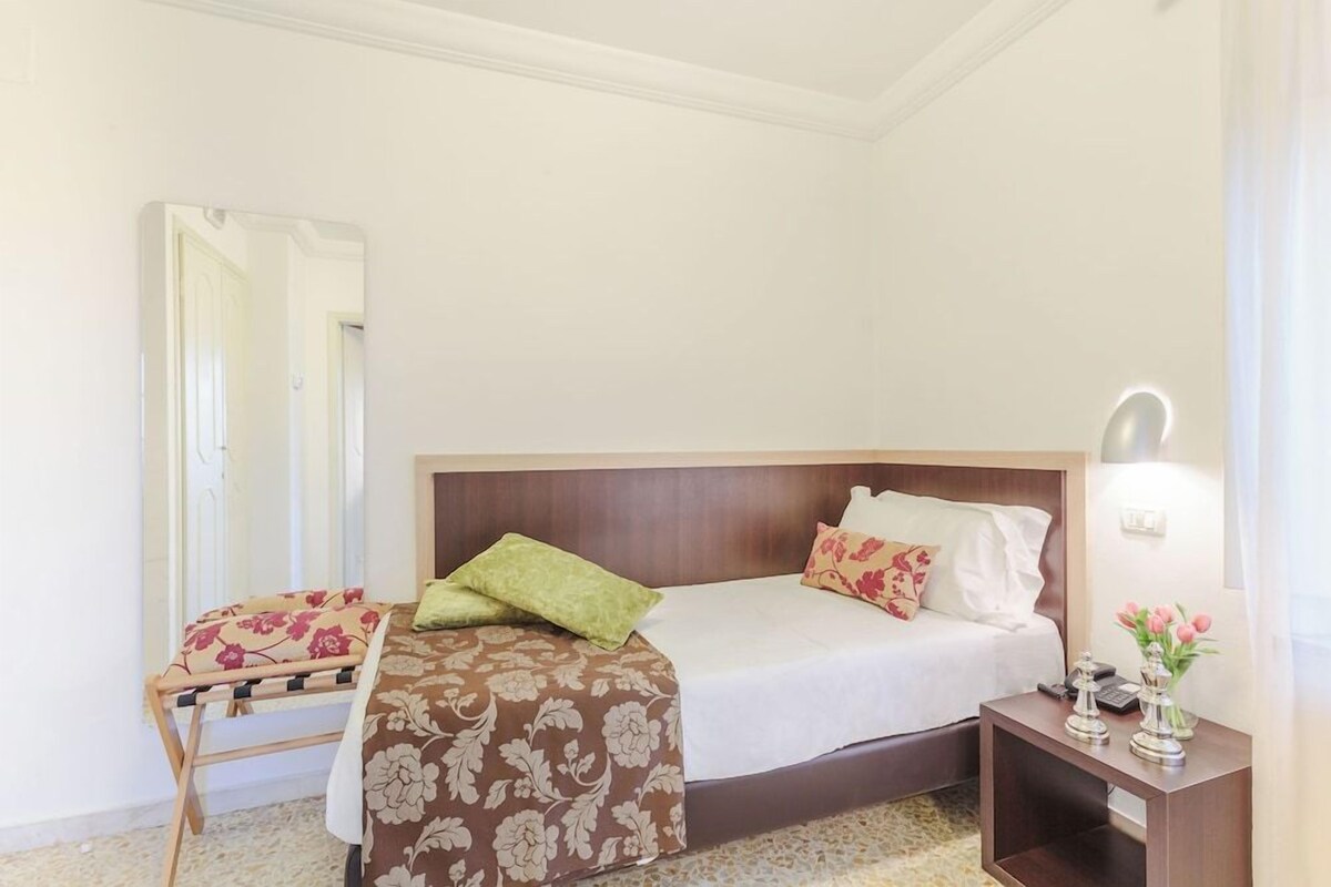 A hotel room with a bed, a bedside table with a lamp, a chair, and a mirror.