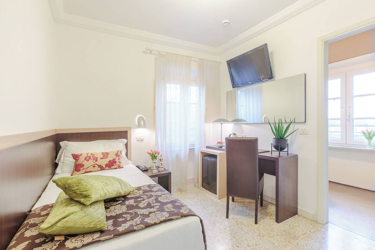 A hotel room with a bed, a desk, a chair, a TV, and a window with curtains.