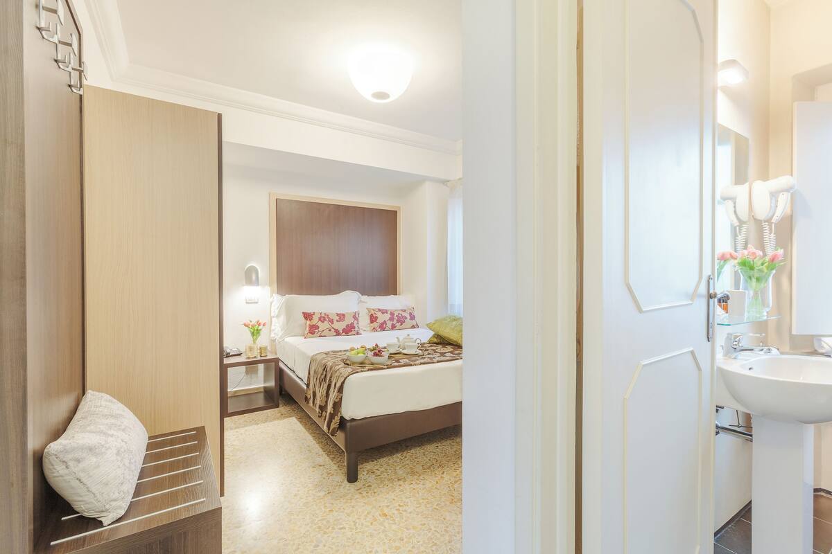 A hotel room with a bed, bedside table, and a bathroom with a sink and mirror.